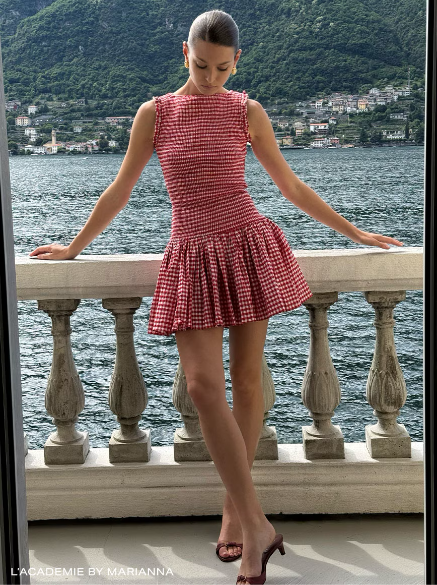 Woman in red checkered dress standing by a lake with mountains.